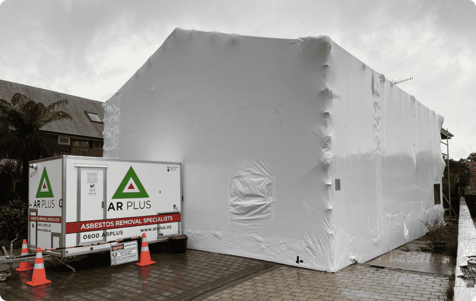 A building with a white plastic covering and an AR Plus trailer parked alongside it.