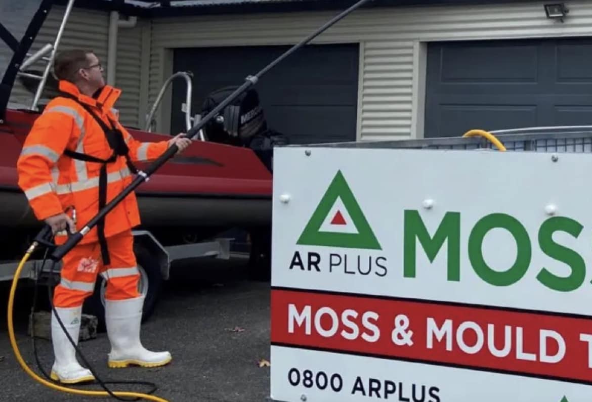 Worker removing mould from a wall using a sprayer with mould remediation chemicals.