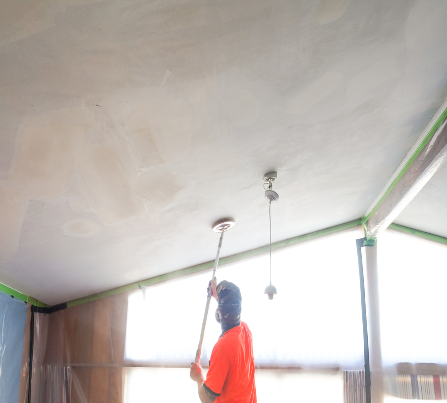 A man painting the black beams of a house white.